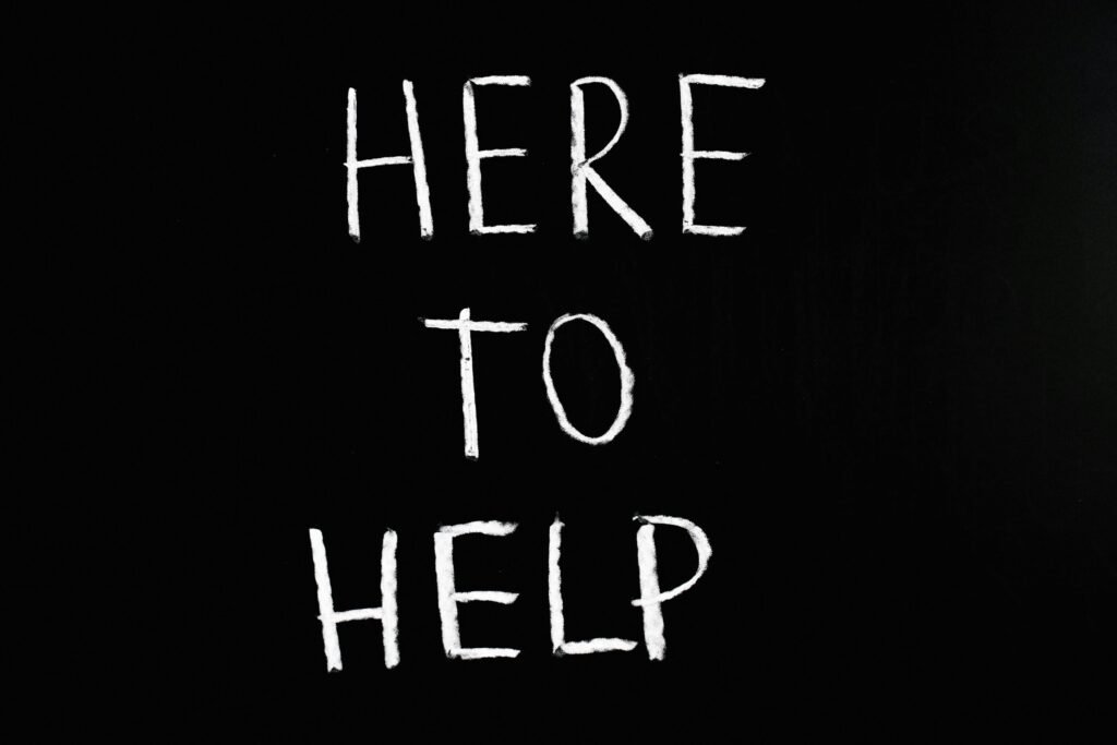 White text 'Here to Help' on a minimalist black chalkboard background, conveying encouragement and support.